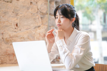 A woman is sitting at a table with a laptop in front of her. She is wearing a white shirt and has...