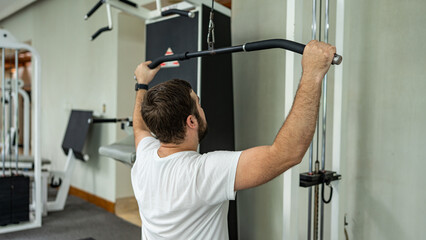 Man performing a lat pulldown exercise at the gym, focusing on back and arm strength training.