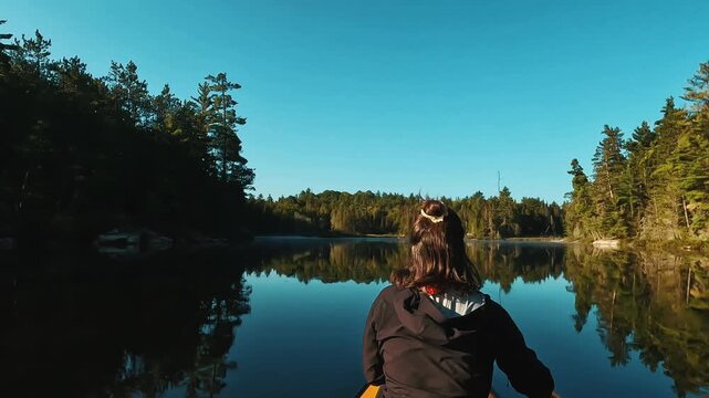 Solo woman paddles a canoe on a calm lake in Temagami, Northern Ontario, surrounded by forest