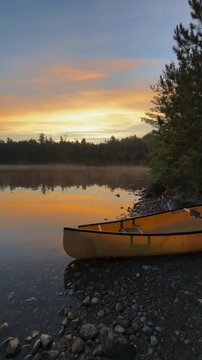 Yellow canoe rests on the rocky shore of a Temagami lake in Ontario at sunset with golden light