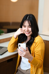 Young woman sitting in cafe looking at  smartphone reading or writing text message.