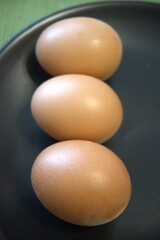 Fresh brown chicken eggs arranged on a black plate, photographed in close up.