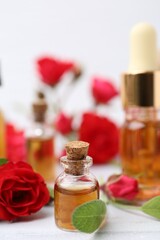 Bottles of essential oil and red roses on white table, closeup
