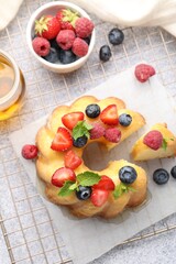 Tasty Bundt cake with berries, honey and mint on light grey table, flat lay