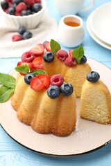 Tasty Bundt cake with berries, honey and mint on light blue wooden table, closeup