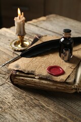 Old paper scroll, book, feather, inkwell and burning candle on wooden table, closeup