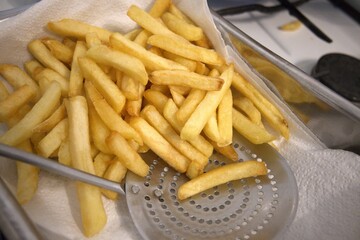 Golden fried potato sticks resting on paper towel in a cooking pot, close up view.