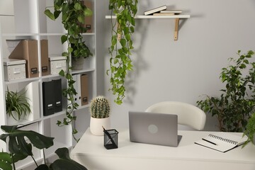 Stylish workplace with laptop, stationery and floral decor in office. Biophilic interior design