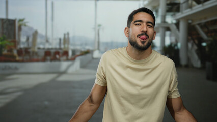 Fototapeta premium Handsome man playfully sticking out tongue standing outdoors in urban street setting surrounded by city architecture suggesting an urban lifestyle