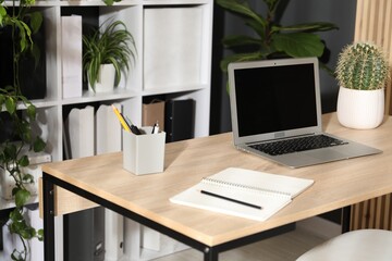 Stylish workplace with laptop, stationery and floral decor in office. Biophilic interior design