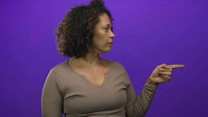Woman with curly hair points index finger to the right in a purple studio side view; confidence guidance.