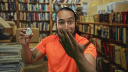 Man holds stopwatch and reaches hand forward in library building while smiling and showing...