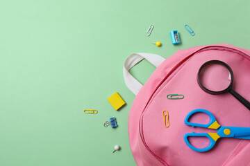 Top view of school supplies arranged around a backpack on a green background. Back to school concept