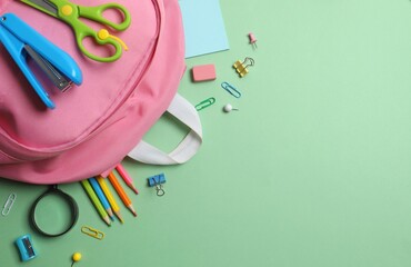 Colorful school supplies arranged around a backpack on a pastel green background. Back to school concept