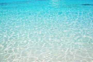 Clear turquoise ocean water with shimmering light reflections and gentle ripples over white sandy seabed, creating a serene tropical sea landscape perfect for evoking tranquil summer vacation, beach t