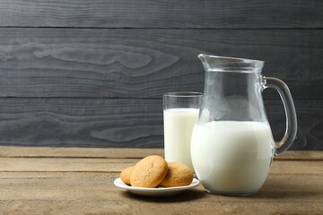 Glass of milk with jug and cookies on table