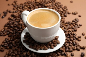 Cup of hot coffee and beans on brown background, closeup
