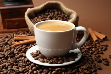 Cup of hot coffee, beans and cinnamon on brown background, closeup
