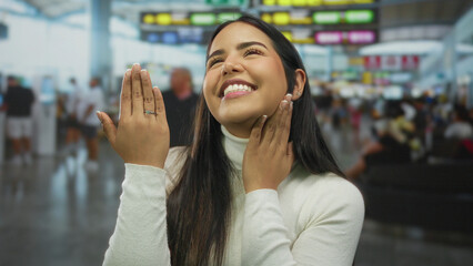 Young woman showing engagement ring joyfully in bustling airport terminal, with bright signs and...
