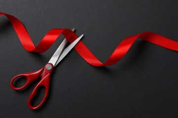 Beautiful red ribbon and scissors on black background, flat lay with space for text. Ceremonial tape cutting