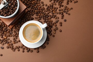 Cup of hot coffee, grinder and beans on brown background, flat lay. Space for text