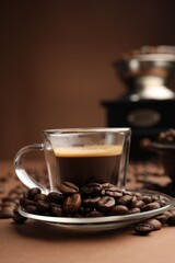 Cup of hot coffee, grinder and beans on brown background, closeup