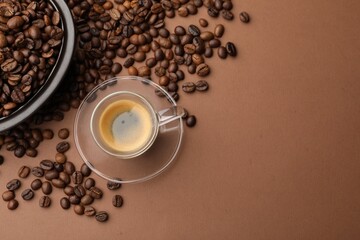 Cup of hot coffee and beans on brown background, flat lay. Space for text