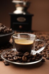 Cup of hot coffee, grinder and beans on brown background, closeup