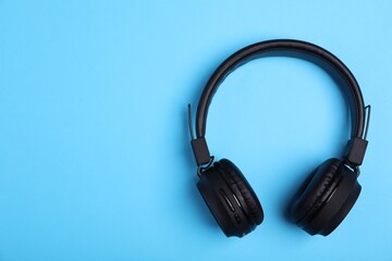 Pair of stylish black headphones on light blue background, top view. Space for text