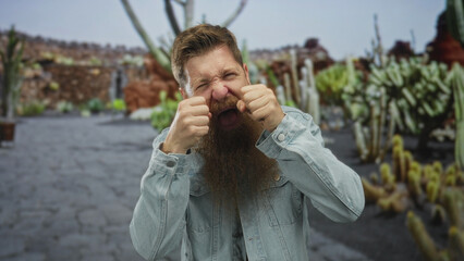 Man mimes crying with fists at eyes and scrunched face on street lined with cactus plants in park;...