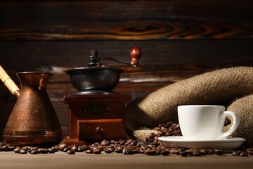Cup of drink, coffee beans, cezve and grinder on wooden table