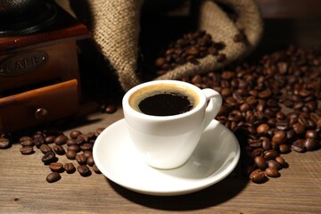 Aromatic coffee in cup, beans and grinder on wooden table, closeup