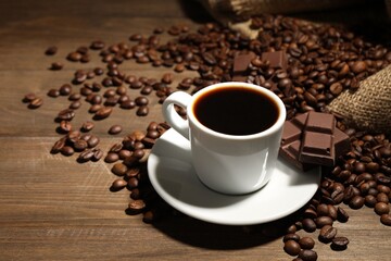Aromatic coffee in cup, beans and pieces of chocolate on wooden table, closeup. Space for text