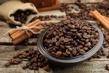 Aromatic coffee beans in bowl and cinnamon on wooden table, closeup