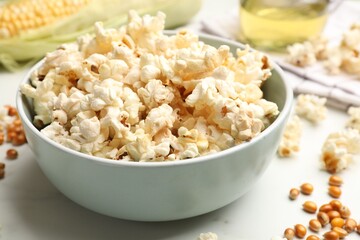 Tasty popcorn and corn kernels on white marble table, closeup