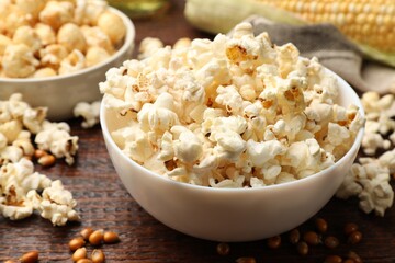 Tasty popcorn and corn kernels on wooden table, closeup