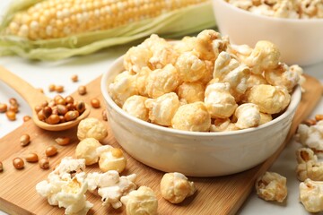 Tasty popcorn, corncob and corn kernels on white table, closeup