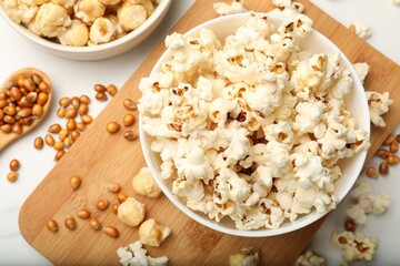 Tasty popcorn and corn kernels on white marble table, flat lay