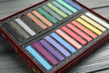 Colorful chalk pastels in box on wooden table, closeup