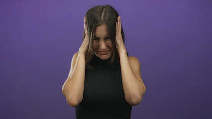 Woman raises hands with open mouth and surprised expression against a purple wall in studio;...