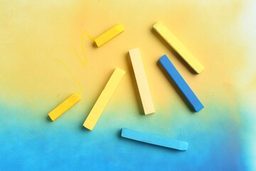 Yellow and light blue chalk pastels on color background, top view