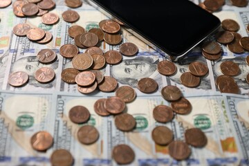 Smartphone and coins on dollar banknotes as background, closeup