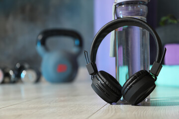 Wireless headphones and bottle of water on floor in gym, closeup. Space for text