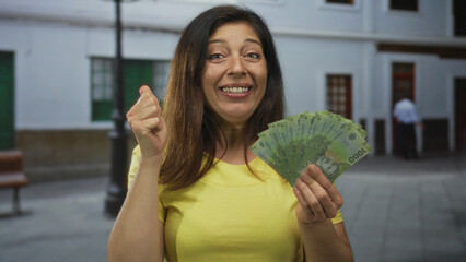 Woman fans a stack of chilean peso banknotes on an urban street while pointing finger upward and...