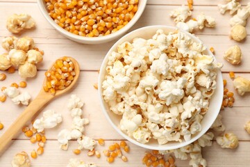 Tasty popcorn and corn kernels on white wooden table, flat lay