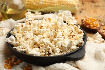 Tasty popcorn, corn kernels, oil and towel on wooden table, closeup
