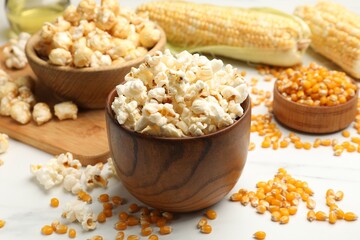 Tasty popcorn and corn kernels on white table, closeup