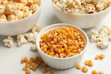 Corn kernels and tasty popcorn on white table, closeup