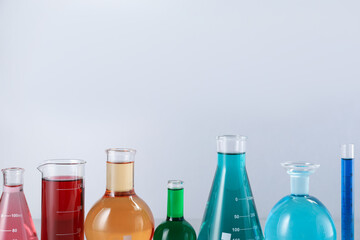 Different laboratory glassware with color liquids on light background. Space for text
