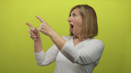 Middle age woman extends bare finger with raised arm pointing forward in lime green studio; curiosity surprise.